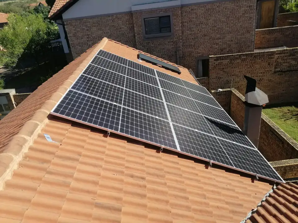 Zonnepanelen op een schuin dak met oranje pannen, van bovenaf gezien, met een schoorsteen ernaast