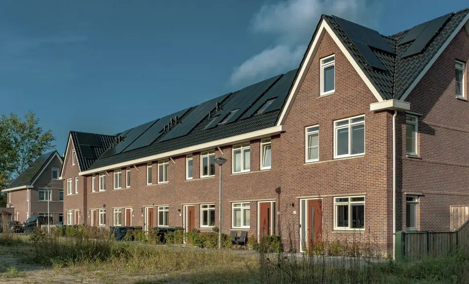 Een nieuwe rij bakstenen eengezinswoningen met donkere daken en zonnepanelen, in de late middagzon